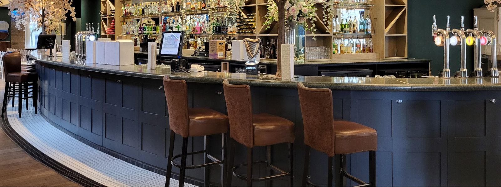 Bar area of Citation, Glasgow, with a wide range of drinks on display, high-back leather stools, blossom trees.