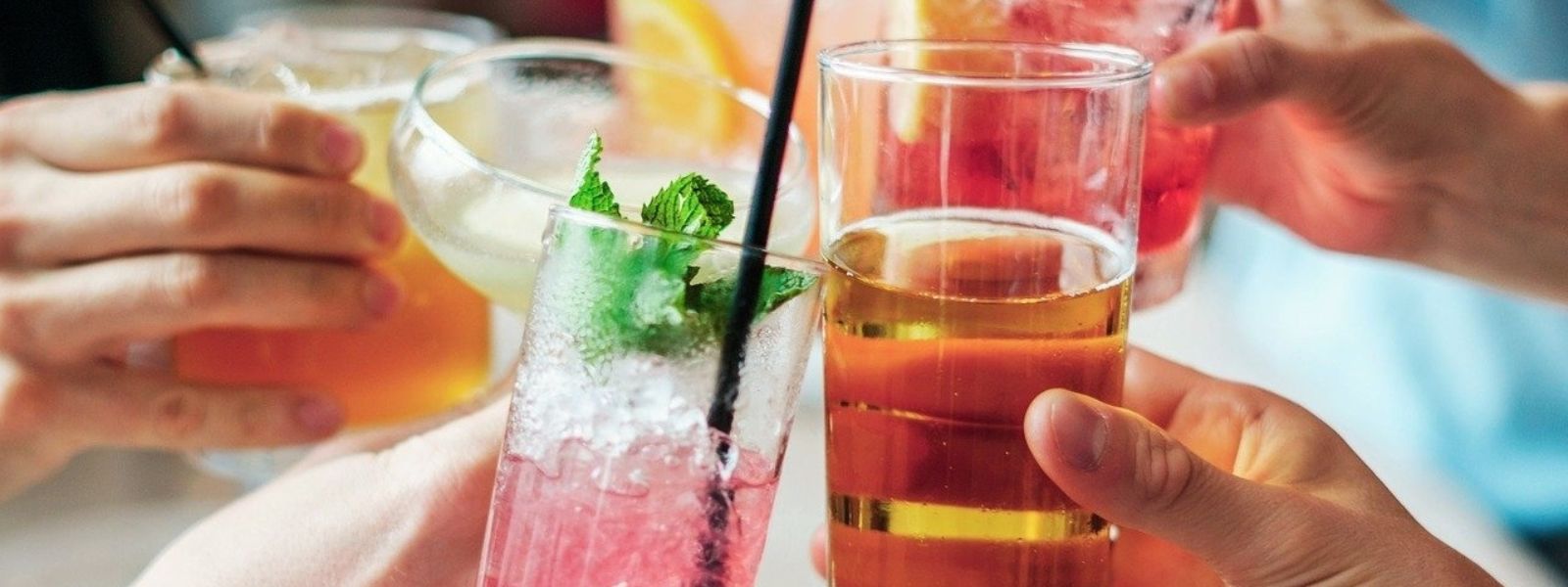Hands holding various drinks, held together in a toast.