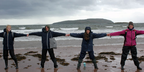 Four students standing on the beach, holding hands, spread out in star shapes