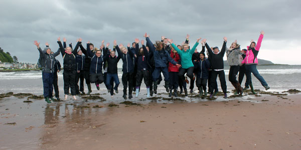 students jumping with their arms up on the beach in Cumbrae