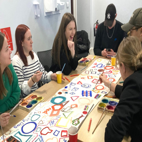 Image of 5 people sitting around a table with colourful drawings in front of them Image of 5 people sitting around a table with colourful drawings in front of them